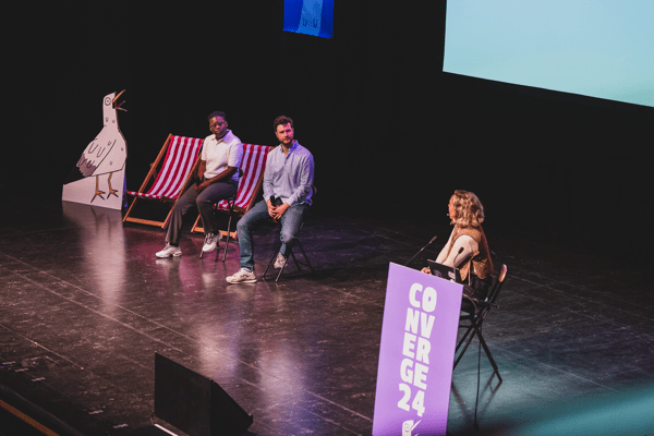 Madelin Snyder delivering her talk at Converge Brighton 2024 with Tim Legeirse and Nef Dukes on stage.