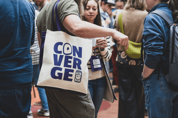 Attendee holding a cream and purple Converge tote bag.